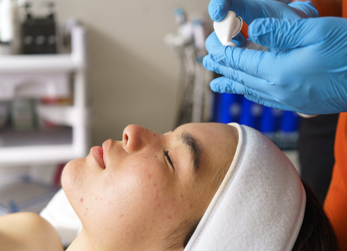 Skincare professional treating acne prone complexion using professional ultrasonic cleansing technique for dermatological improvement